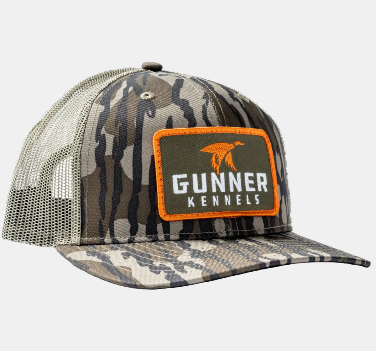 The BOTTOMLAND MALLARD TRUCKER by GUNNER is a Mossy Oak Bottomland camo mesh hat with an orange and black patch featuring a retriever above the brand name on front.