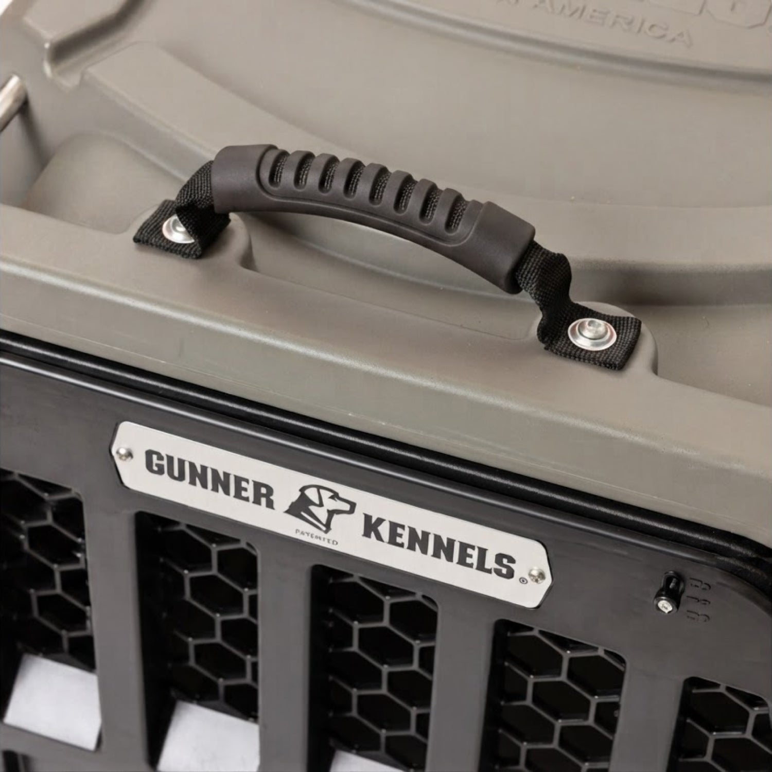 Close-up of the durable GUNNER pet crate, featuring a BLACK KENNEL HANDLE on top and a metal Gunner Kennels label secured to the front with screws. The door showcases a unique hexagonal pattern, mirroring the toughness of its Food Crate 30 sibling.