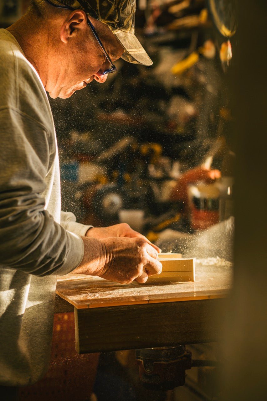 Charles Jobes stands at a work bench in his shop carving a duck decoy.