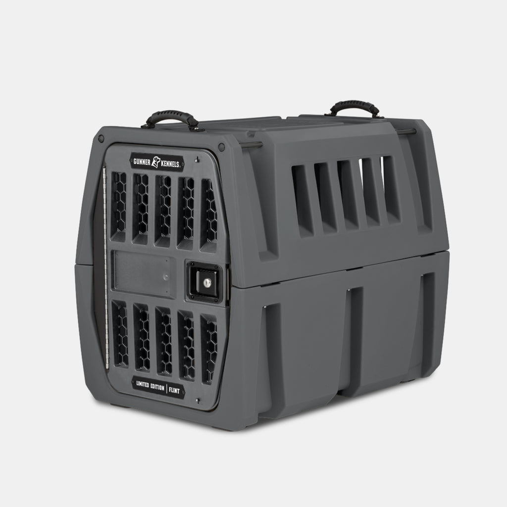 The GUNNER G1™ KENNEL - FLINT is a rugged, dark gray pet crate with ventilation slits, honeycomb-patterned door vents, black handles, and a secure latch—designed for durability—shown against a plain white background.
