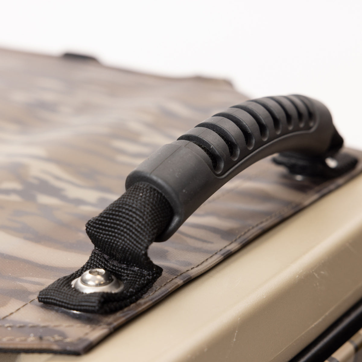 Close-up of a black, ribbed plastic handle secured with metal rivets to the camouflage-patterned GUNNER ALL-WEATHER KIT 2.0 MOSSY OAK BOTTOMLAND, designed to provide UV protection in any environment.