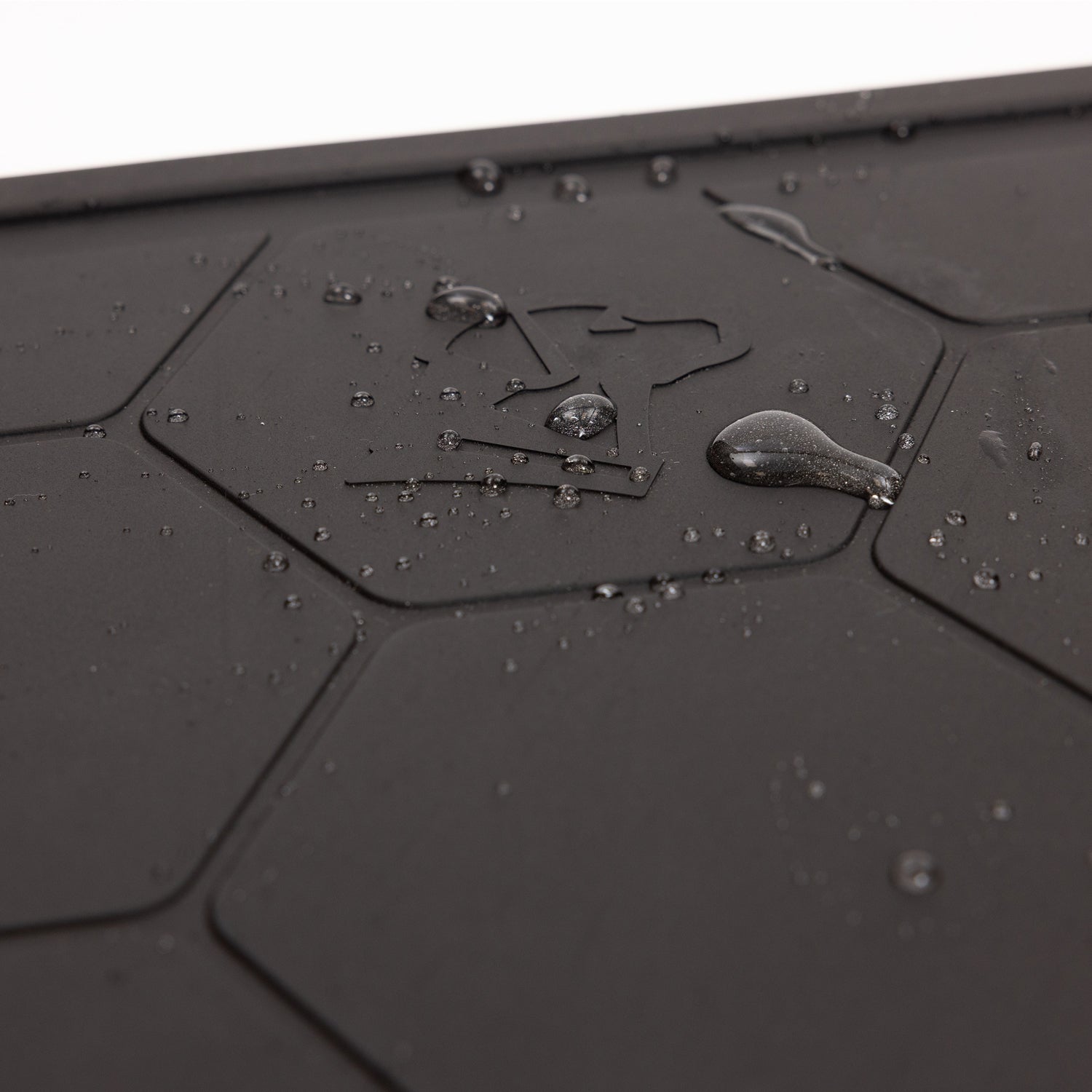 Close-up of water droplets on the GUNNER BOWL MAT - BLACK, featuring hexagonal patterns and an umbrella symbol that indicates its slip-resistant and water-resistant properties.
