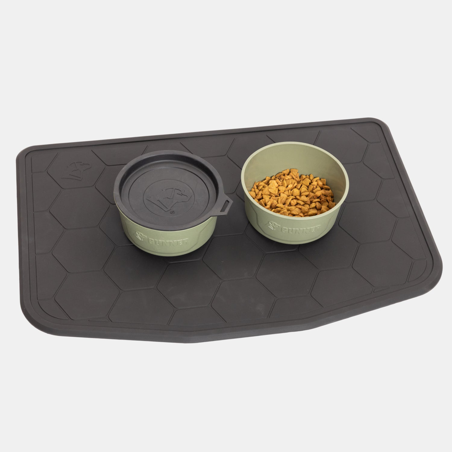 Two green pet bowls—one with a lid and the other filled with kibble—rest on the GUNNER BOWL MAT - BLACK, which features a large hexagonal pattern. This slip-resistant mat keeps your pets’ mealtime tidy and prevents bowls from sliding out of place.