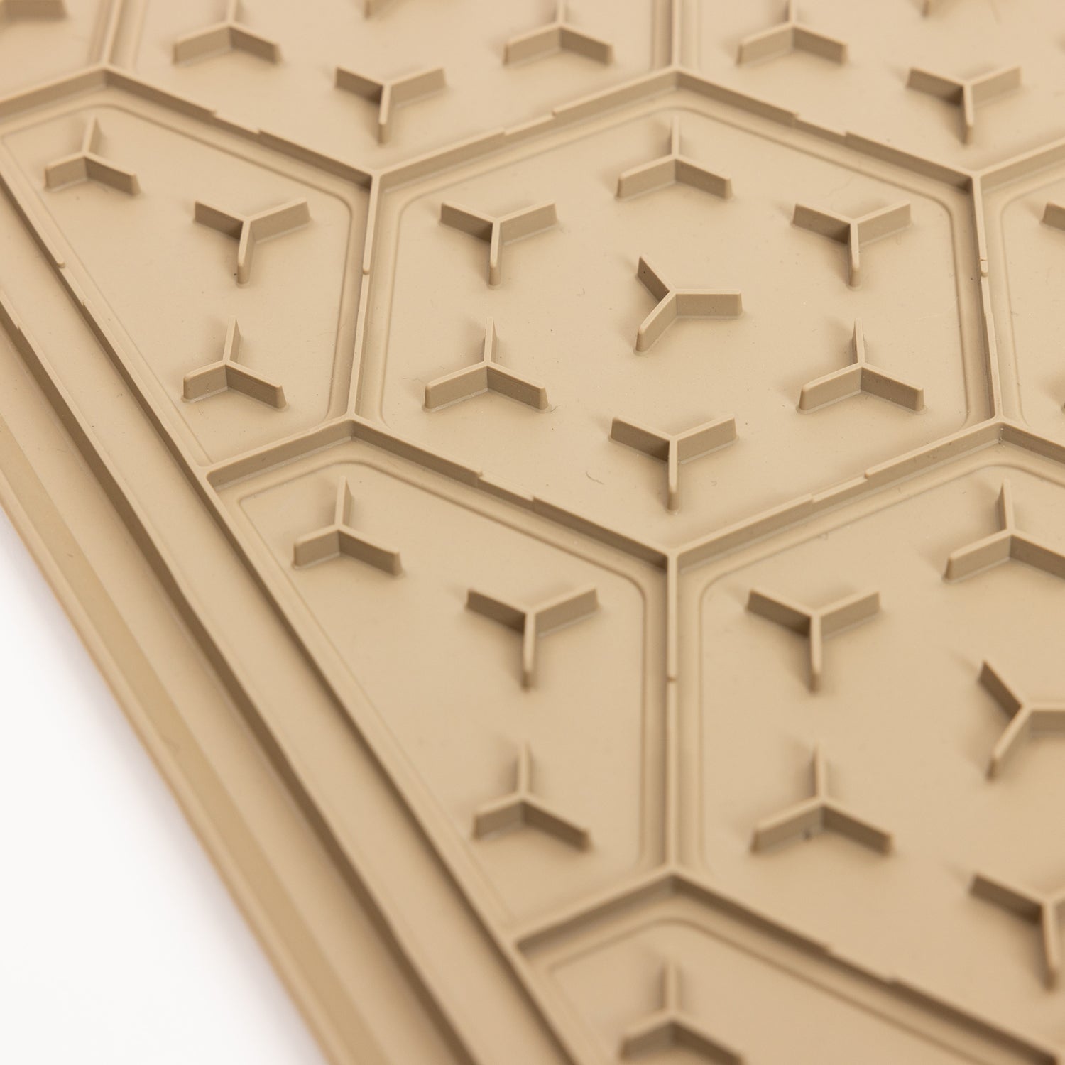 A close-up of the GUNNER BOWL MAT - TAN shows its textured surface featuring hexagonal patterns with small, three-pronged raised shapes inside each hexagon, all designed to be slip-resistant and dishwasher-safe.