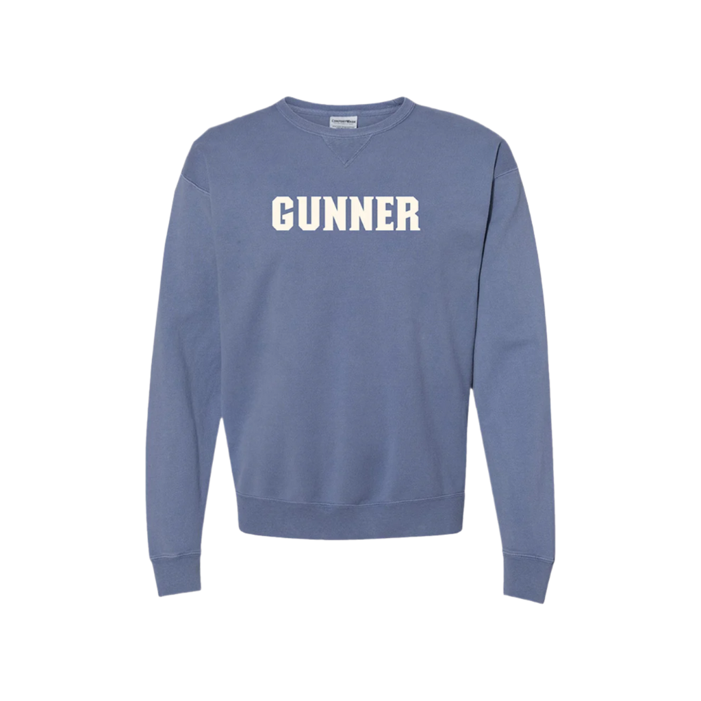 The GUNNER Crewneck, by GUNNER, is a warm, thick blue sweatshirt with “GUNNER” in bold white letters across the chest. Wind resistant for extra comfort. Displayed on a plain white background.