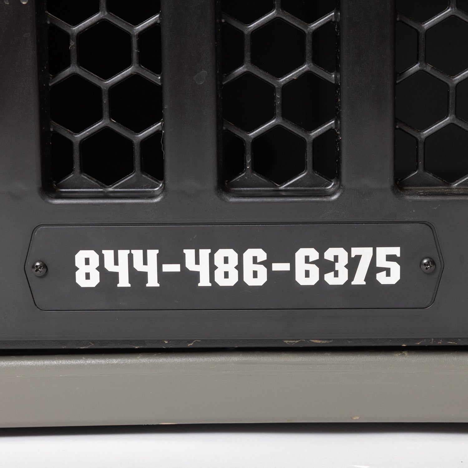 A GUNNER PERSONALIZED KENNEL DOOR TAG is displayed on a black, honeycomb-patterned surface, featuring the phone number 844-486-6375 in bold white numbers.