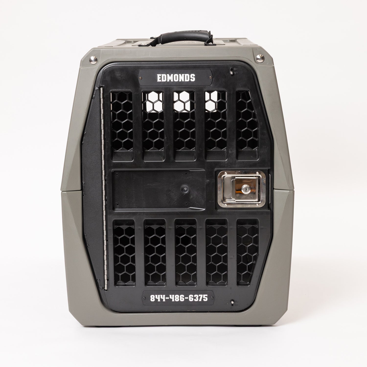 A sturdy gray and black pet crate with a hexagonal vent pattern, carrying handle on top, metal latch, and the words EDMONDS and 844-486-6375 displayed on the front—perfect for pairing with the GUNNER PERSONALIZED KENNEL DOOR TAG for easy identification.