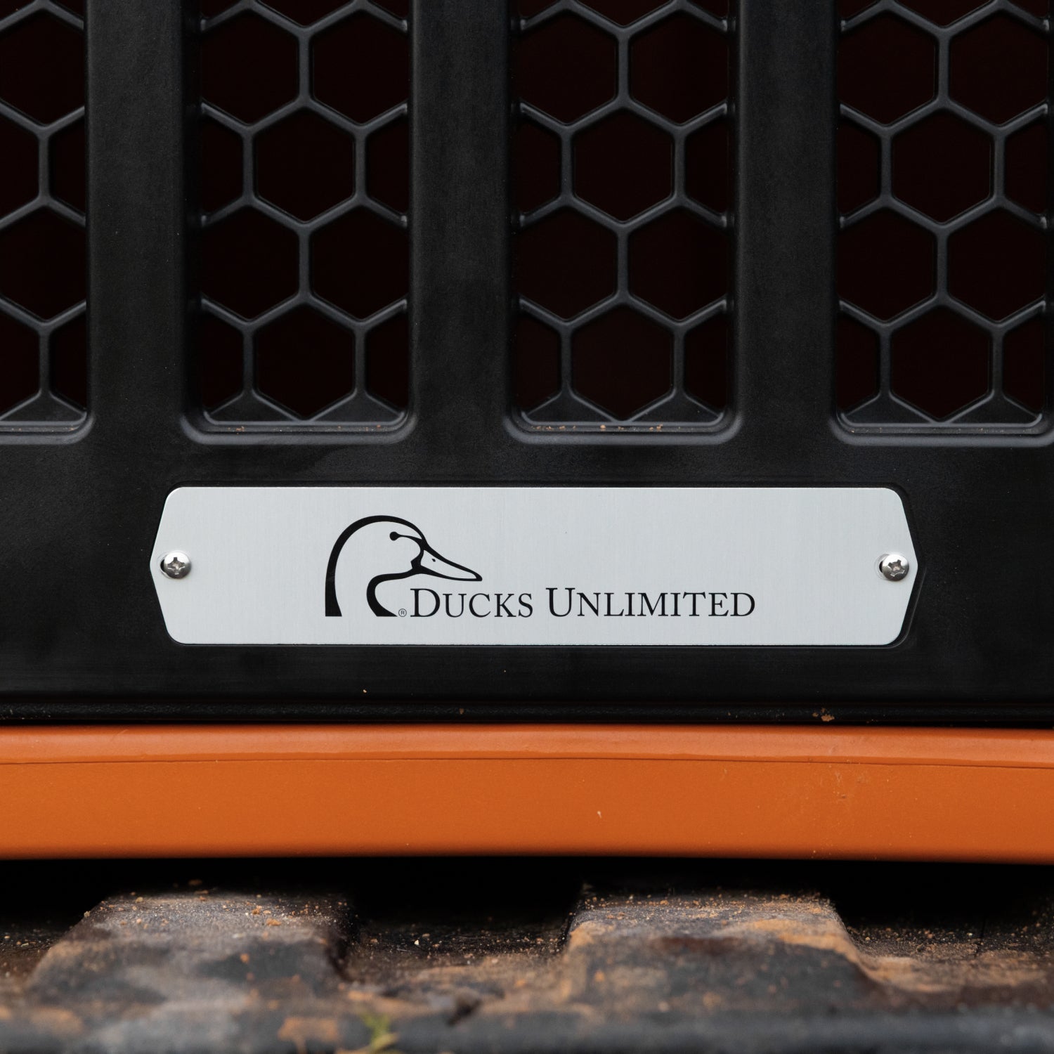 The GUNNER G1™ KENNEL - Ducks Unlimited Orange features a metal plate with the Ducks Unlimited logo on a black honeycomb-vented panel above an orange base, showcasing its premium and safe dog crate design.