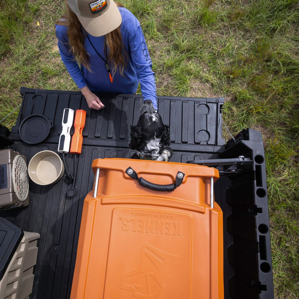 Person with a dog in a truck bed featuring a Gunner Kennel, Bumper, Food Bowl, Food Crate and Turtlebox speaker.