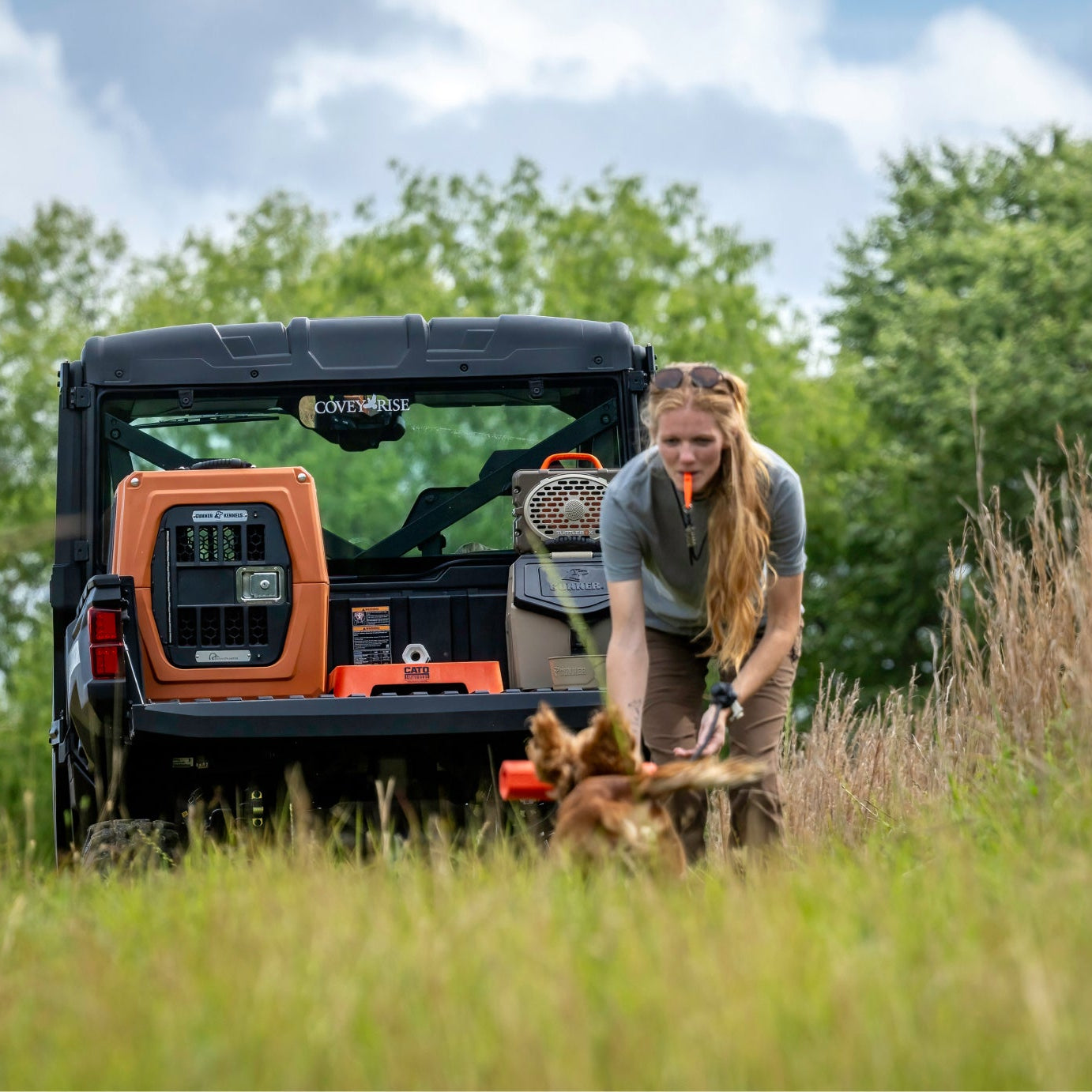 Person with a dog near an off-road vehicle in a natural setting featuring a GUNNER kennel in Ducks Unlimited Orange