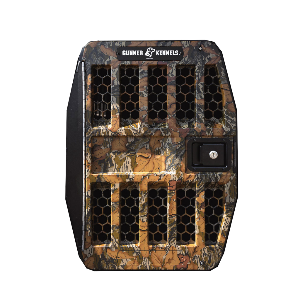 A camo-patterned Gunner Kennels pet crate door with black hexagonal vents and a built-in lock, designed for the safety of your working or hunting dog, shown against a white background.