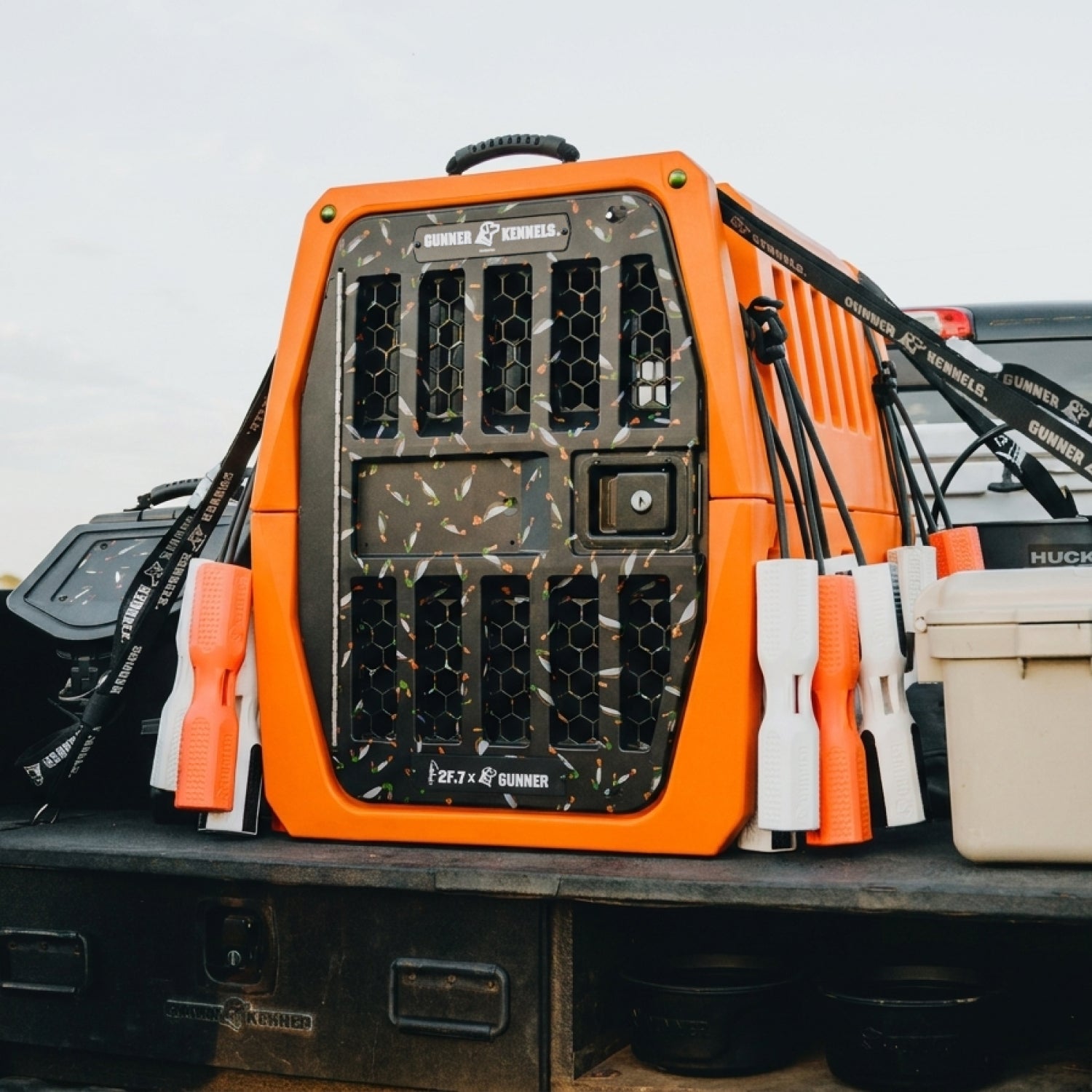 The GUNNER G1™ KENNEL - 2F.7 ORANGE CRUSH, featuring black vented doors and handles, sits on a vehicle among outdoor gear, providing industry-leading shock protection for your dog’s safest travel crate experience.