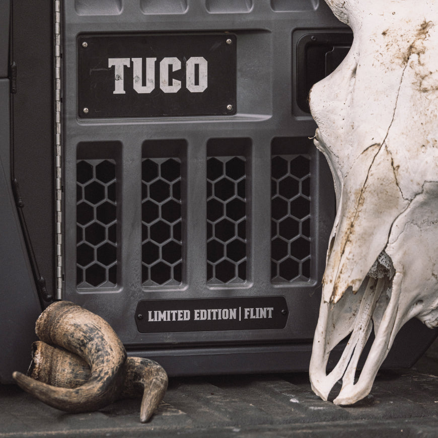 A close-up of the rugged GUNNER G1™ KENNEL - FLINT beside a large animal skull and curled horn creates a rustic, outdoorsy scene with limited edition style, perfect for adventure.