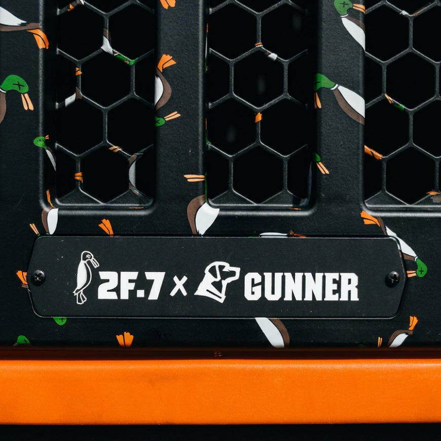 Close-up of the GUNNER G1™ KENNEL - 2F.7 ORANGE CRUSH, a black double-walled panel with honeycomb vents, flying duck illustrations, 2F.7 x GUNNER label, and duck and dog head icons for ultimate shock protection.