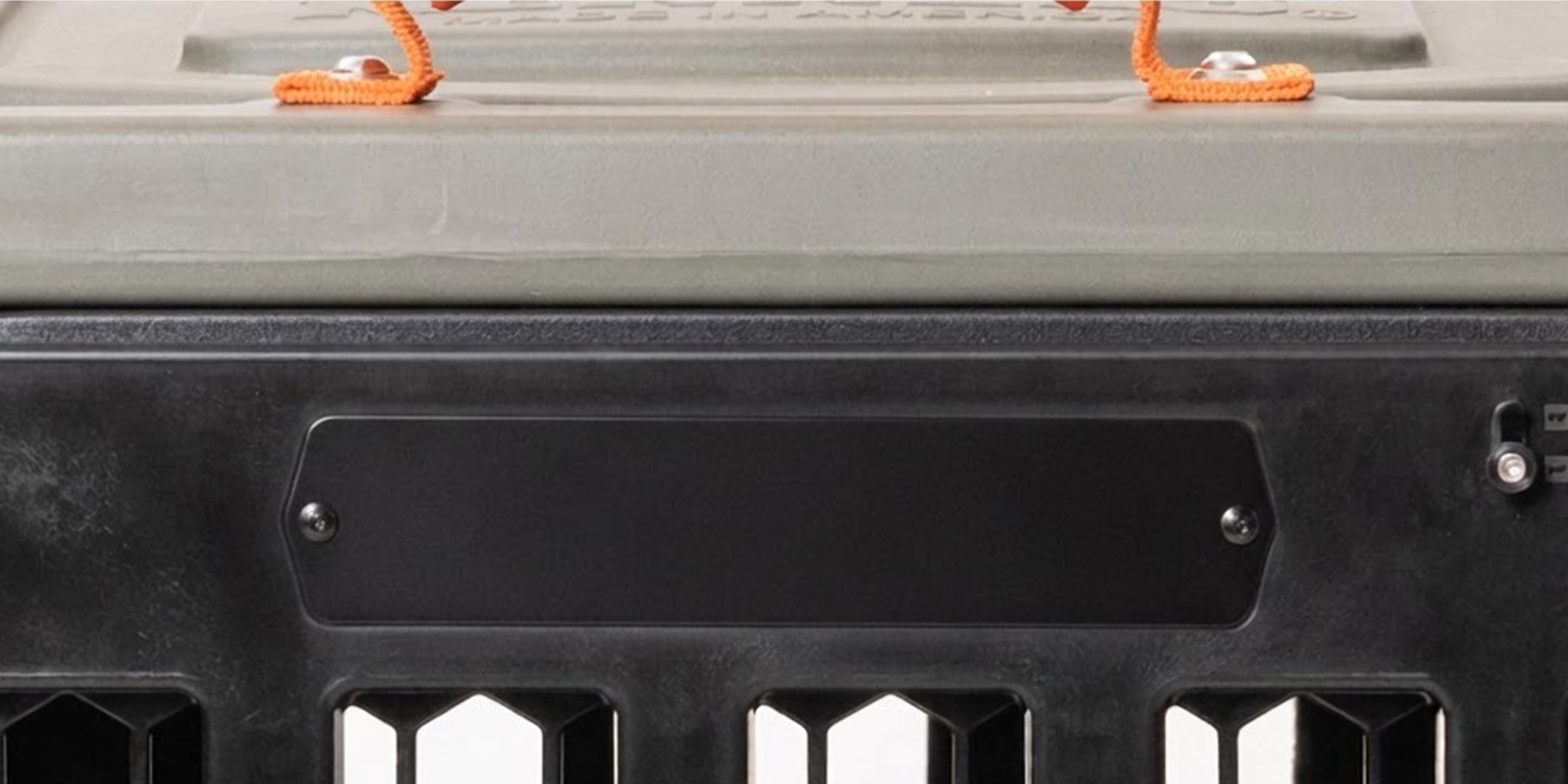 Close-up of a gray and black plastic dog kennel or crate with an attached lid, two orange ropes on top, and a blank rectangular label area on the front. The lower section has hexagonal vent openings, making it ideal for transporting hunting dogs or other working dogs safely and securely.