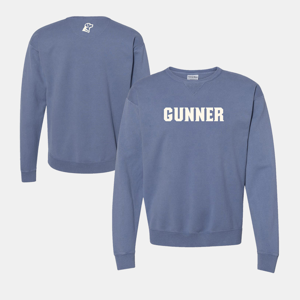 A blue crewneck sweatshirt with GUNNER printed in bold white letters on the front, inspired by quality outdoor gear. Features a small white graphic on the upper back near the neck. Both front and back views are shown.