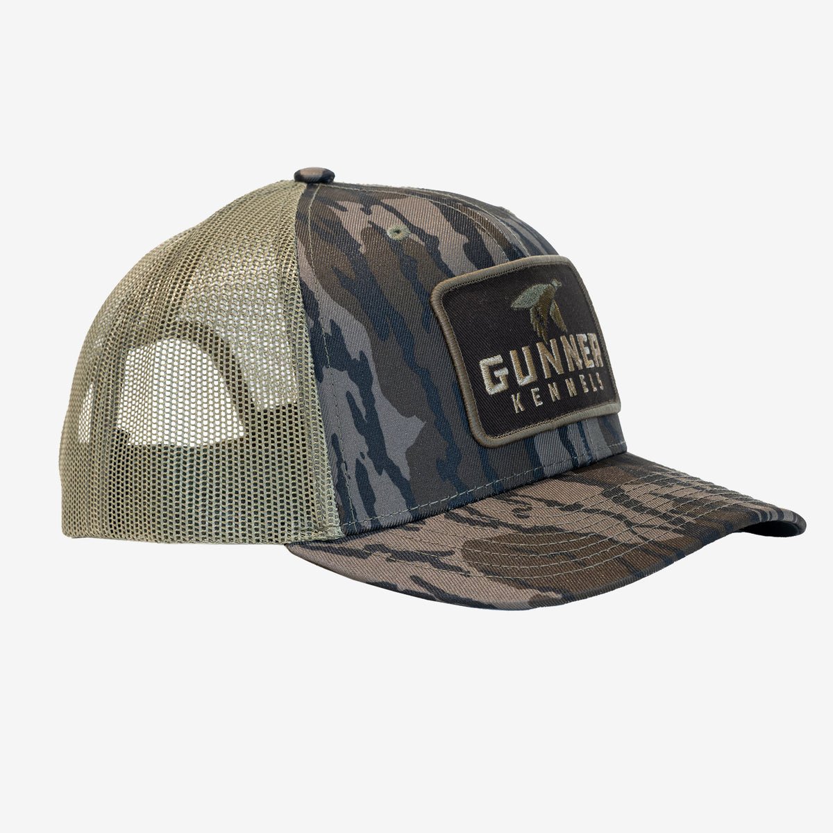 BOTTOMLAND MALLARD TRUCKER hat with a Mossy Oak Bottomland pattern, a tan mesh back, and a rectangular patch featuring a duck silhouette and the text GUNNER KENNELS.