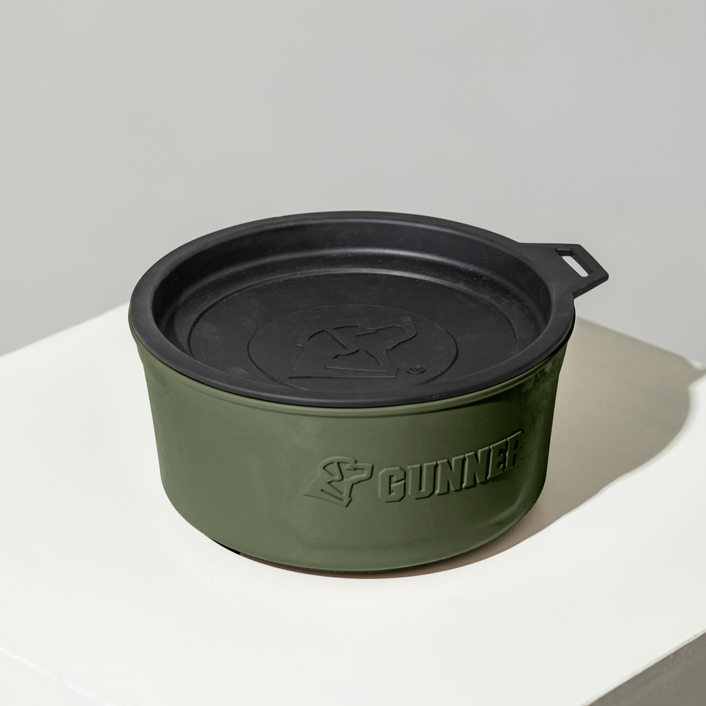 The GUNNER DOG BOWL - GUNNER GREEN by GUNNER is a round, green and black bowl with a fitted spill-proof lid and embossed dog logo, shown on a white surface—proudly made in America.