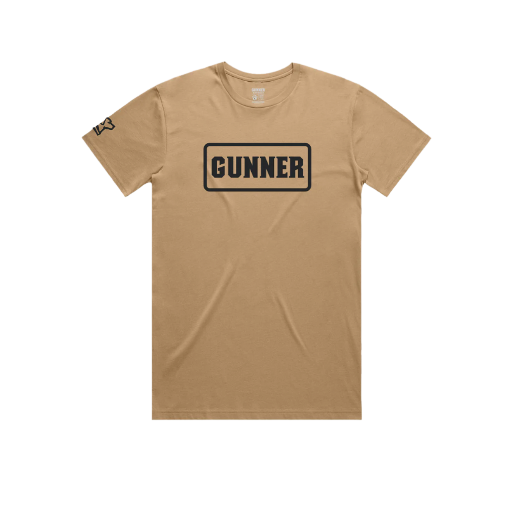 The GUNNER Pack Tee by GUNNER is a tan, heavyweight short-sleeve shirt with GUNNER in bold black letters inside a rectangular border on the chest and a small black graphic on the left sleeve.