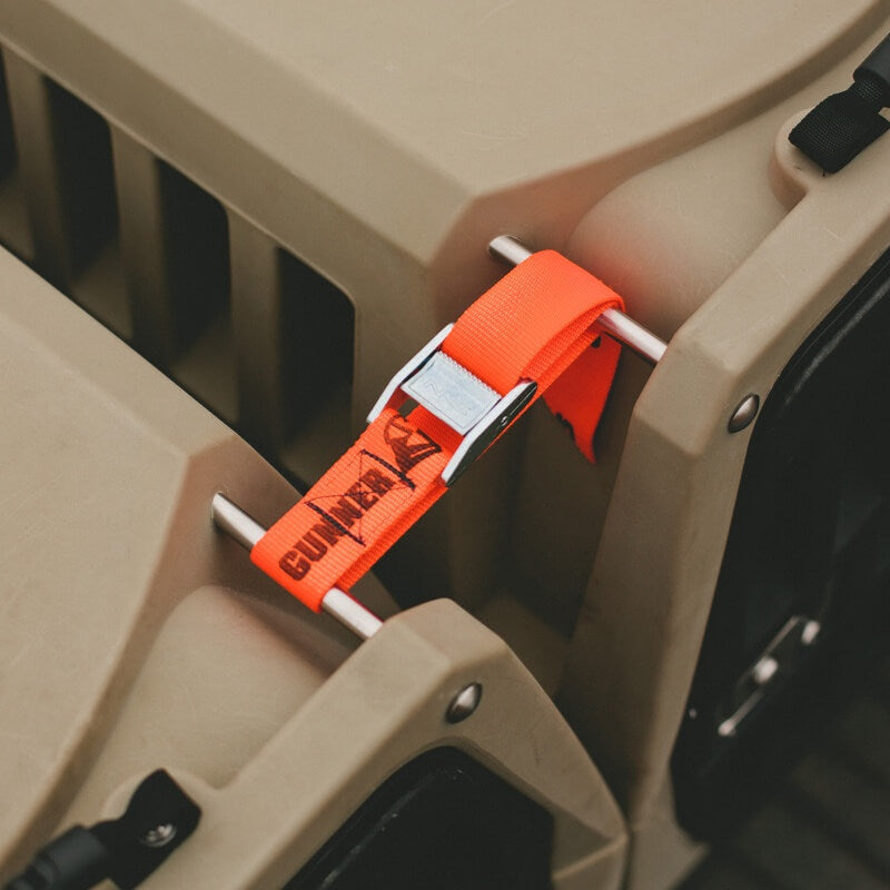 Close-up of an orange GUNNER CONNECTION STRAP KIT with a metal buckle securing two tan crates. The strap displays the black GUNNER logo and text, showing its use as part of the Connection Strap Kit.